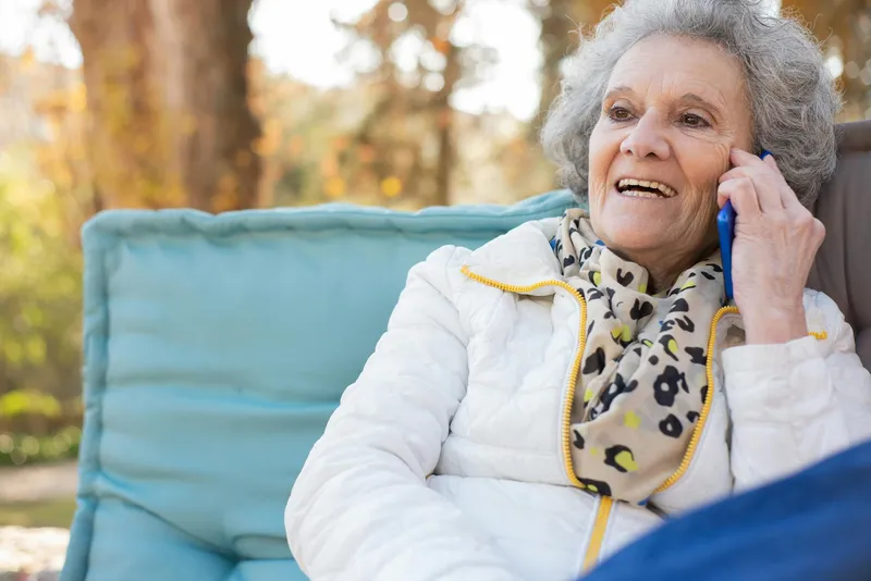 An elderly woman sitting outside, talking on the phone